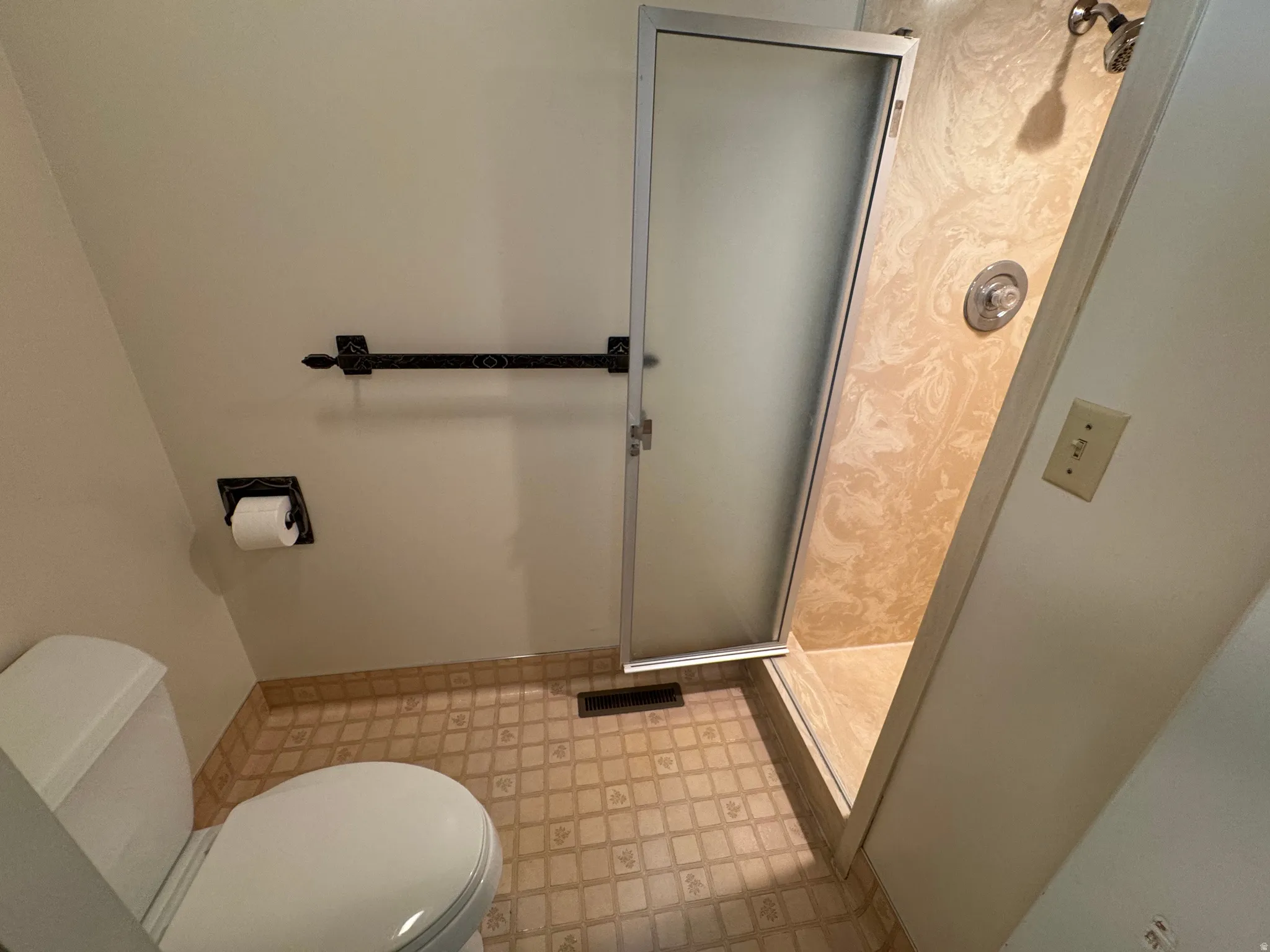 Bathroom featuring a shower with a frosted glass door, a toilet, patterned floor tiling, and wall-mounted fixtures