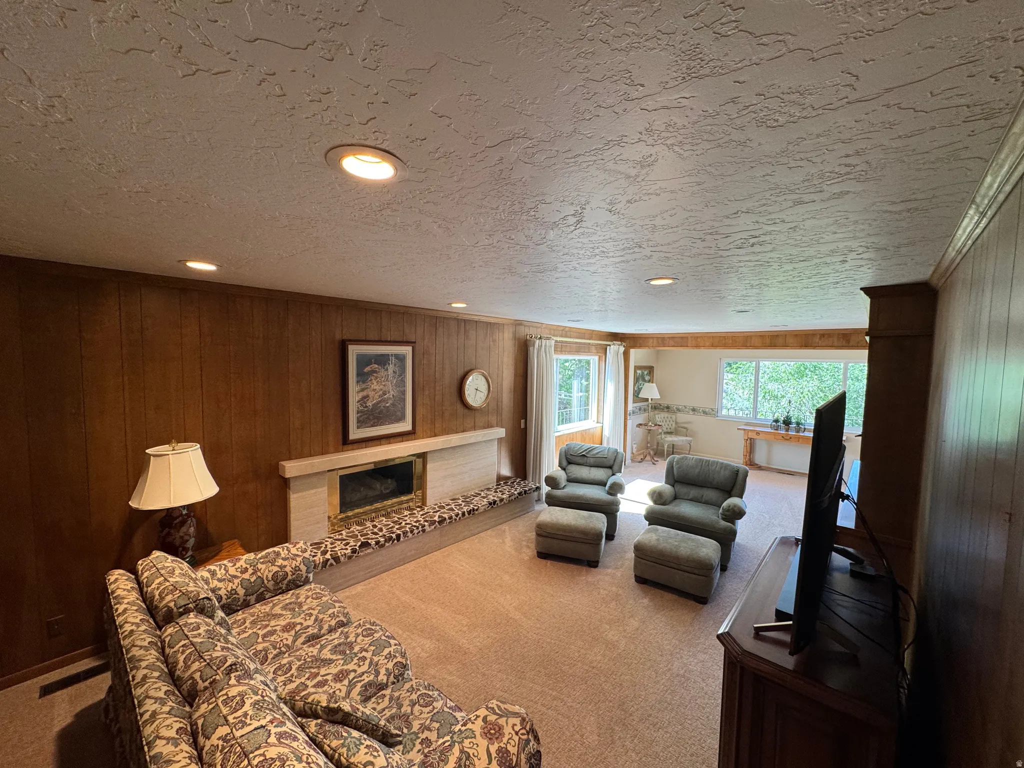 Spacious room featuring wood paneling, recessed lighting, and a prominent fireplace with a stone surround