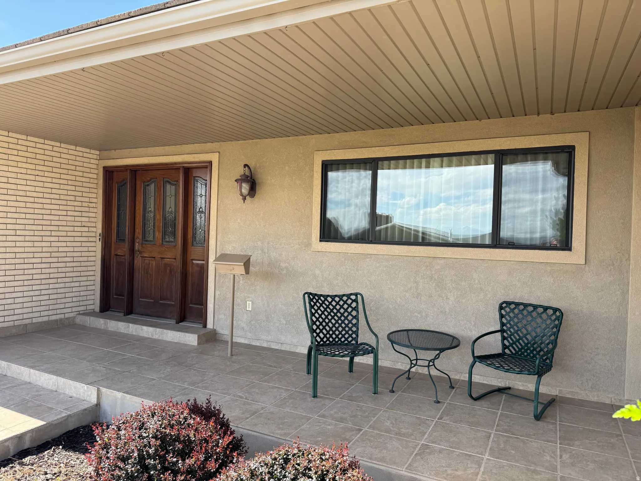 Covered front porch featuring a wood-finish double entry door with decorative glass panels, a stucco exterior, and a tiled porch surface