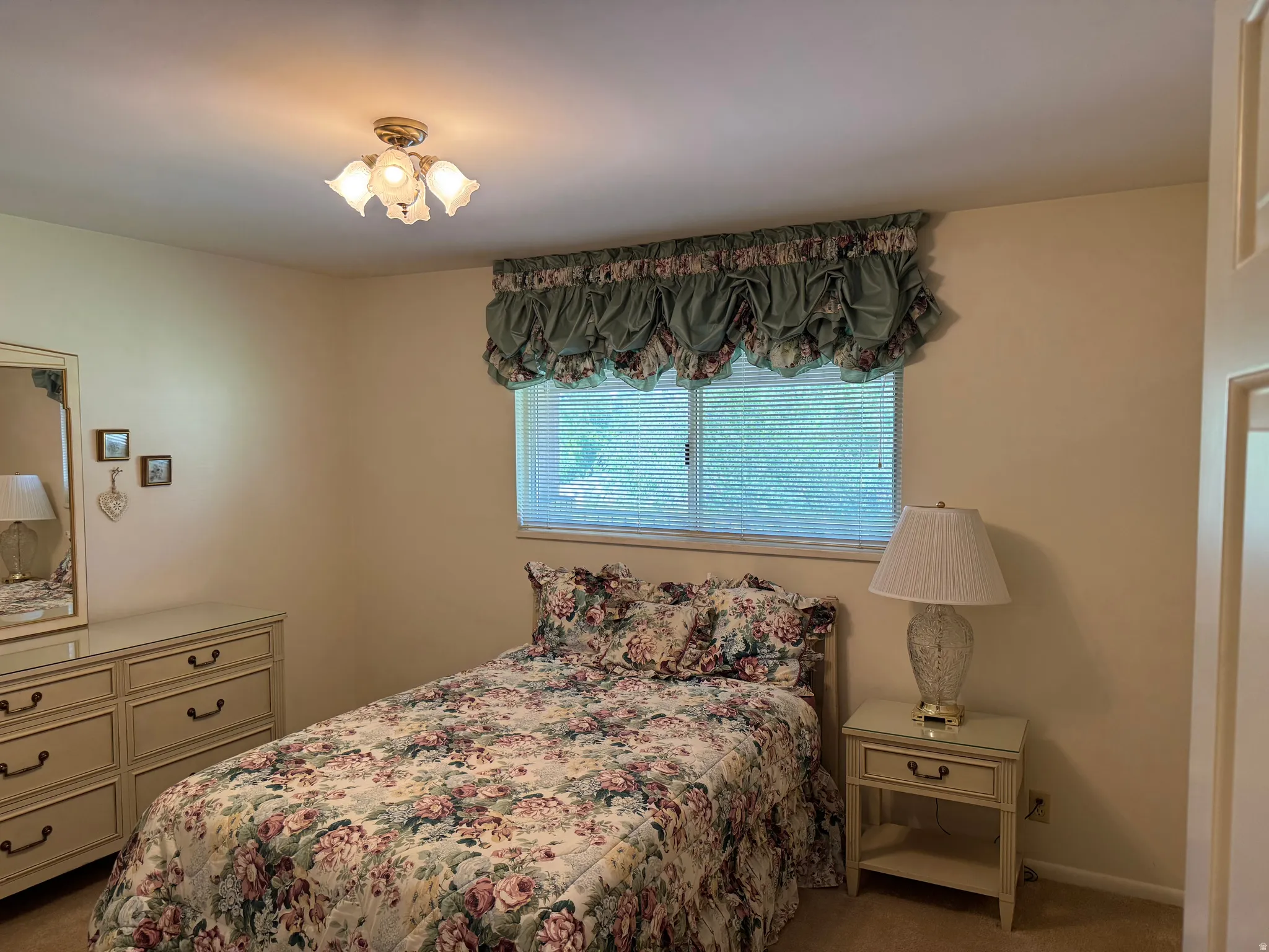 Carpeted room featuring a window with blinds, a multi-bulb ceiling light fixture, and neutral-toned walls