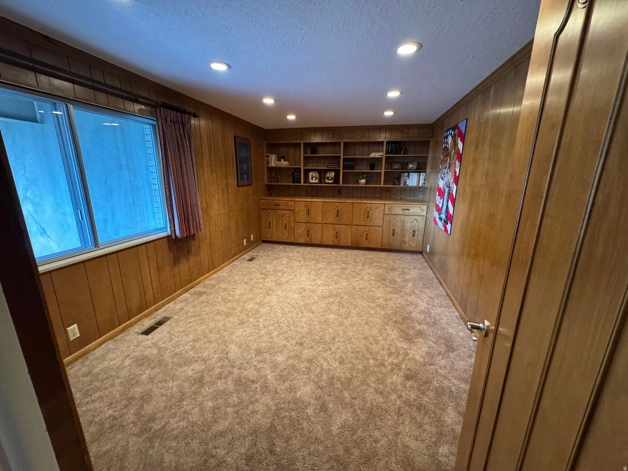 Room featuring wood paneling, built-in shelving, integrated cabinetry, recessed lighting, and a window