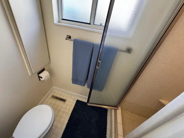 Compact bathroom featuring a white toilet, frosted glass window, and a shower with a sliding door