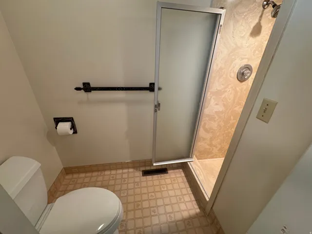 Bathroom featuring a shower with a frosted glass door, a toilet, patterned floor tiling, and wall-mounted fixtures