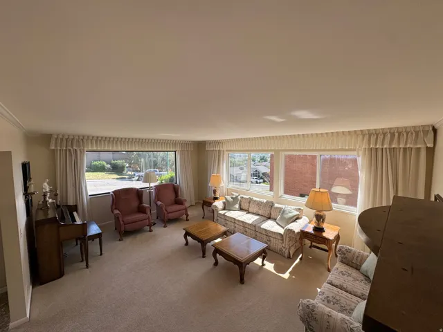 Spacious living area featuring expansive windows, neutral carpeting, and crown molding