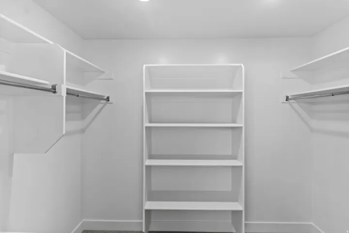 Walk-in closet featuring white built-in shelving, hanging rods, and recessed lighting