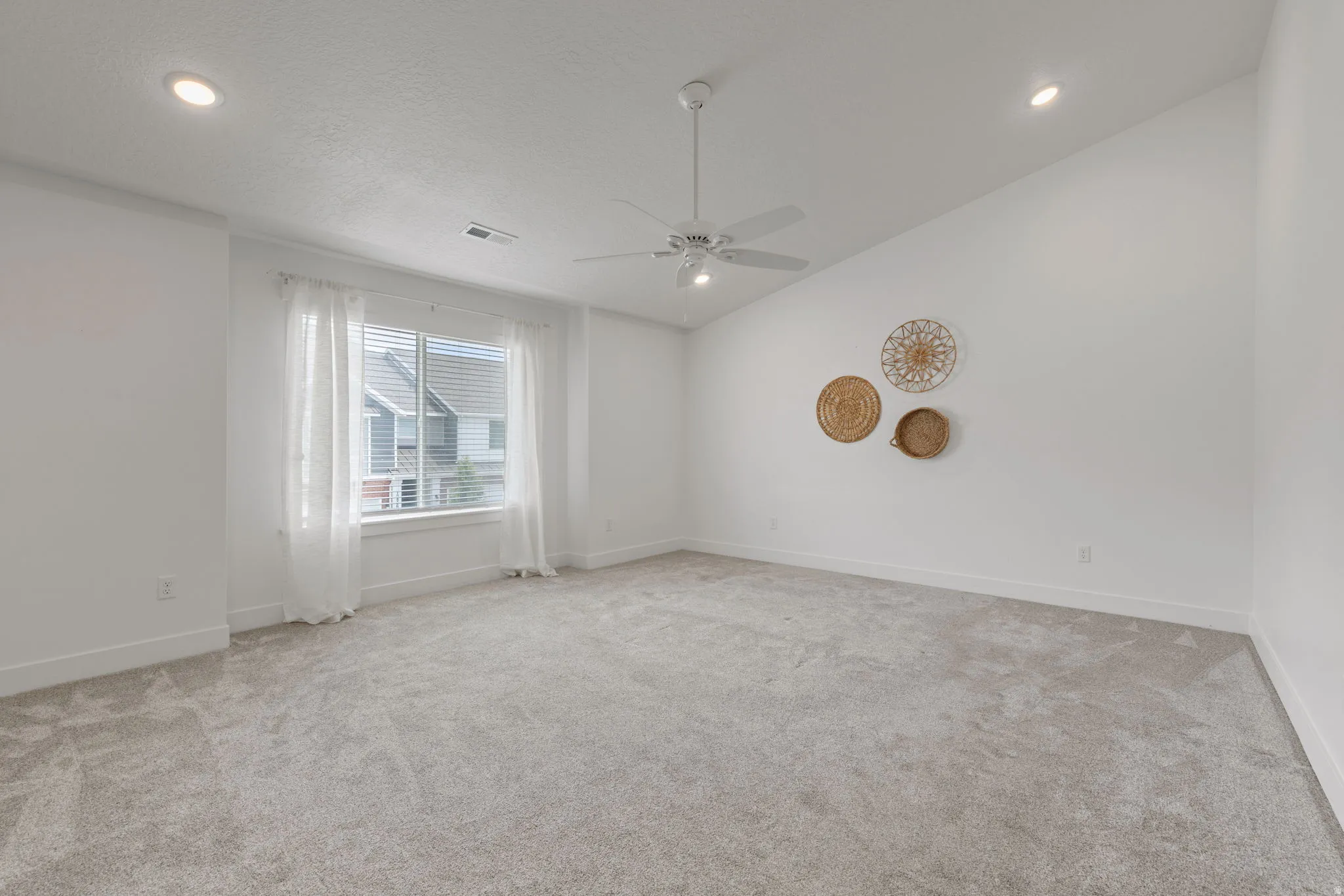 Spacious room featuring vaulted ceilings, recessed lighting, a ceiling fan, light gray carpeting, and a window with blinds and sheer white curtains