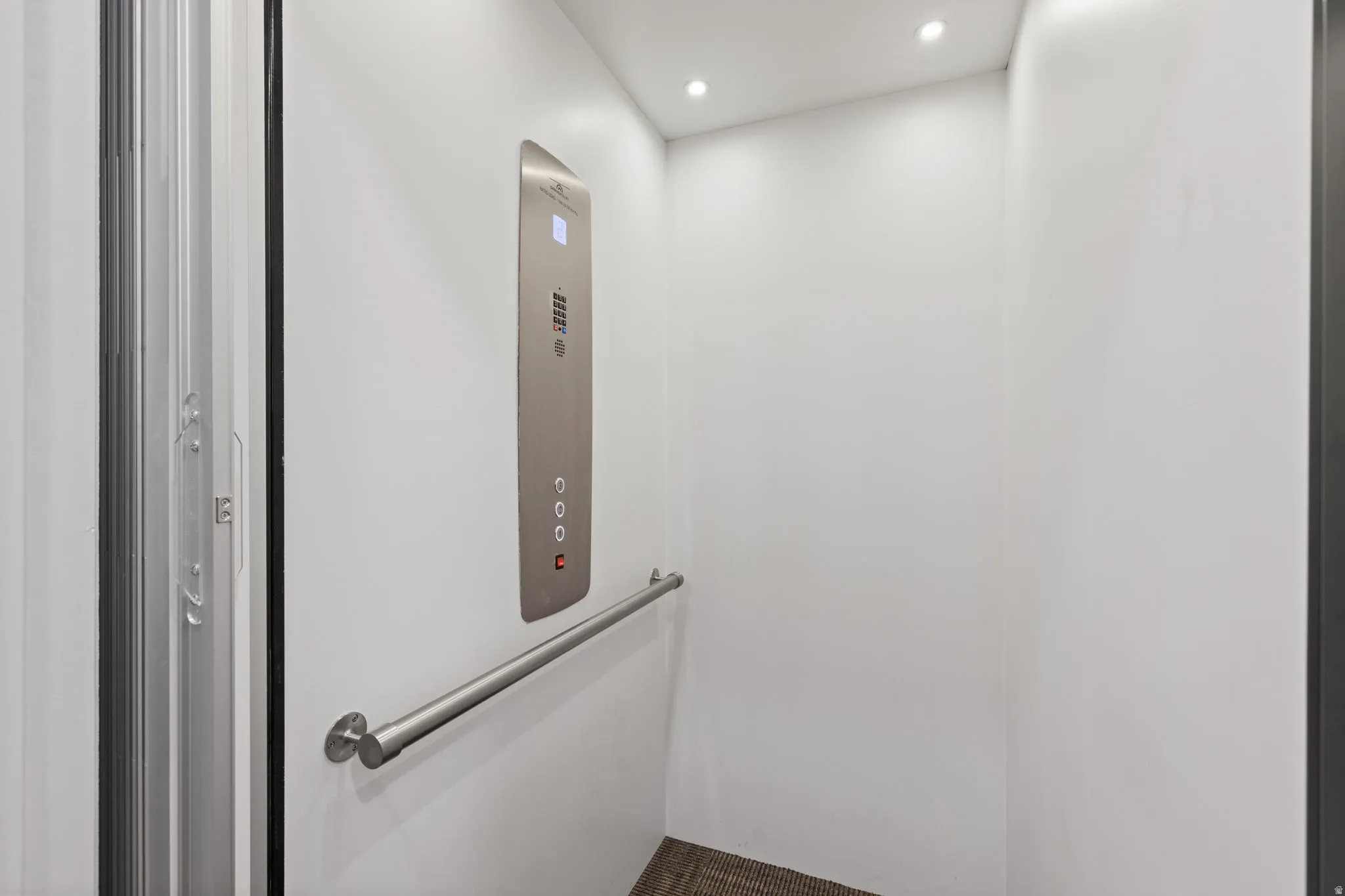 Residential elevator featuring a brushed metal control panel, recessed lighting, and a stainless steel grab bar