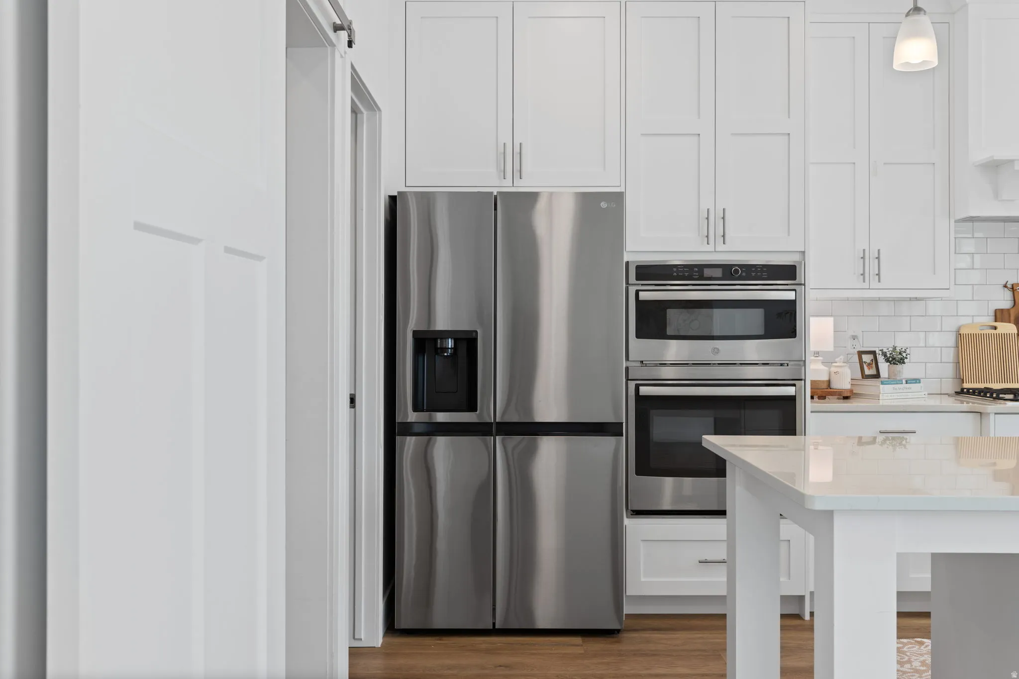 Kitchen featuring stainless steel appliances, white shaker-style cabinetry, wood-finish flooring, a white subway tile backsplash, and a light-colored countertop