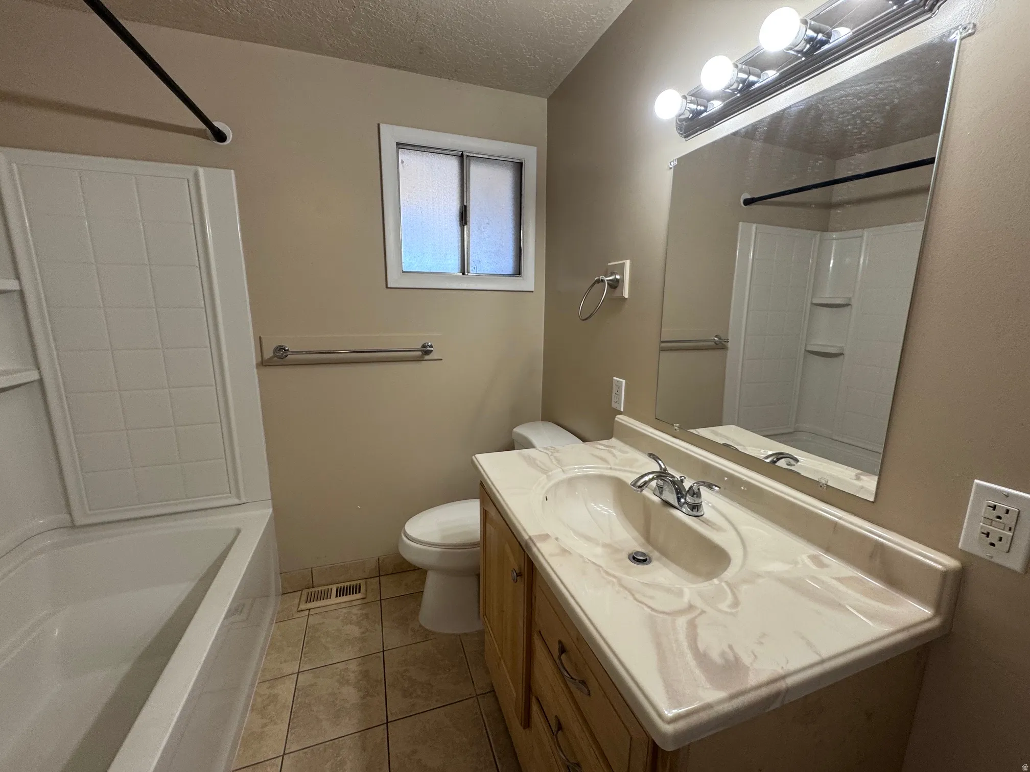 Bathroom featuring a single vanity with wood-finish cabinetry, a large mirror, and a tub/shower combination with a tiled surround