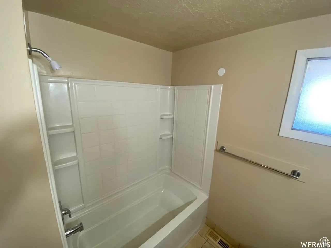 White bathtub and shower combination unit featuring integrated shelving