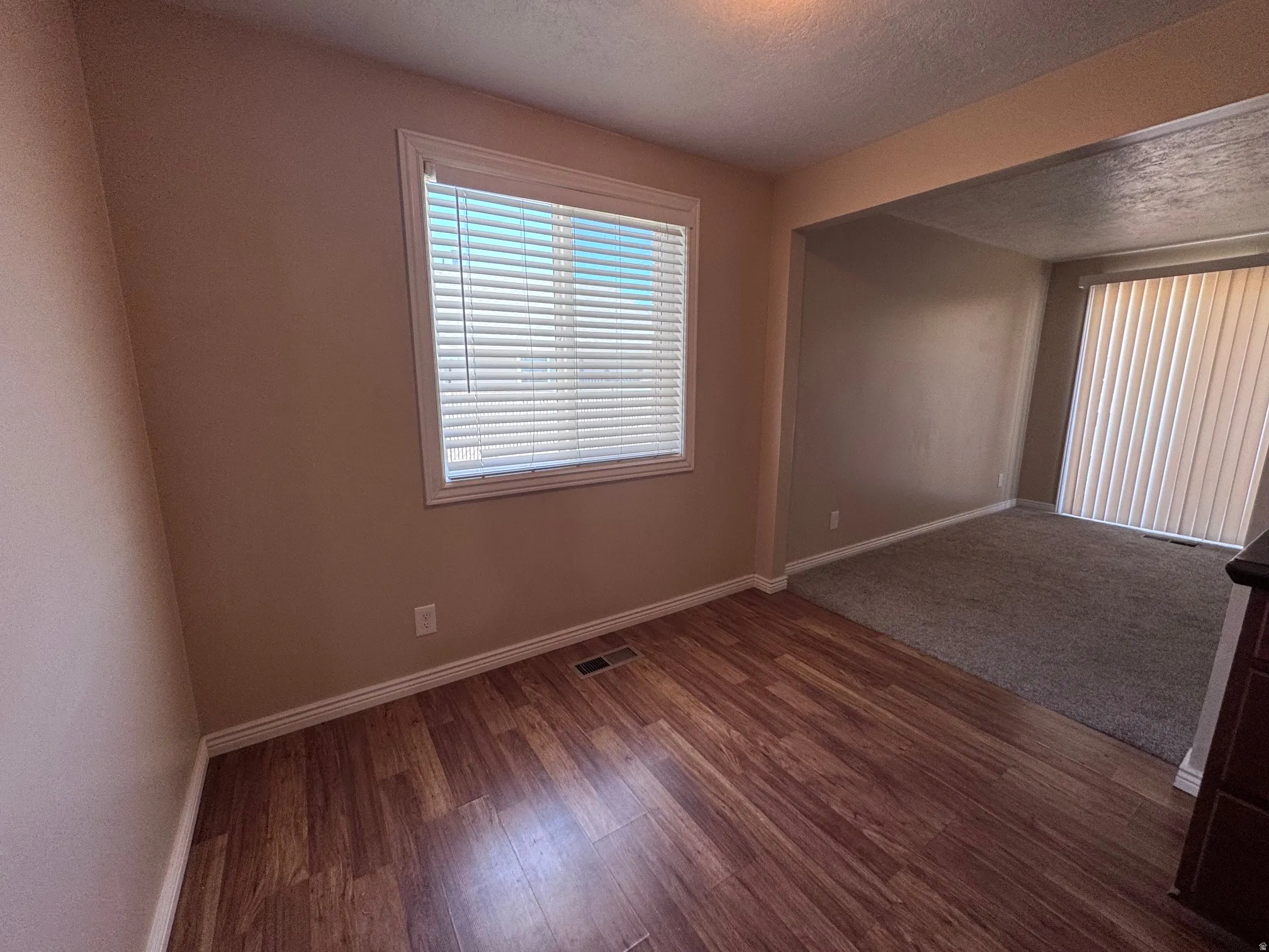 Wood-finish flooring in a neutral-toned room with a window featuring white blinds