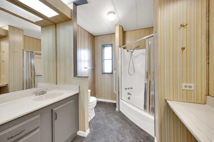 Master bathroom featuring a white bathtub with a shower kit and glass enclosure, a white toilet, and a vanity with a white countertop and grey cabinetry