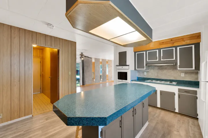 Kitchen featuring a large central island with a blue speckled countertop, integrated cooktop, wall oven, and wood-finish flooring