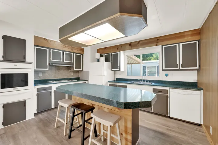 Kitchen featuring a central island with a countertop, wood-finish flooring, built-in double oven, paneled cabinetry, and a double-basin sink
