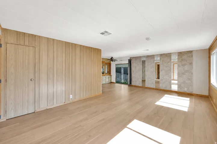 Spacious room featuring light wood-finish flooring, vertical wood paneling, and a mirrored accent wall