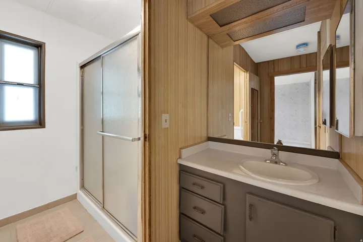 Bathroom featuring a vanity with an oval sink, an overhead mirrored medicine cabinet, a sliding glass shower enclosure, a window with frosted glass, and tile flooring