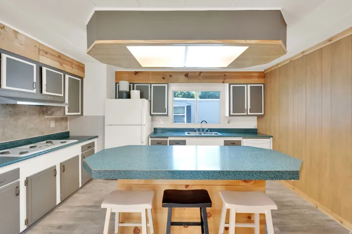 Kitchen featuring a central island with a speckled countertop, perimeter cabinetry with wood accents, and a built-in range