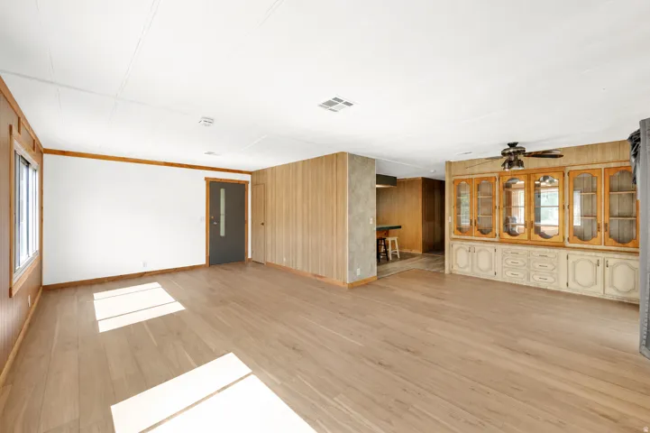 Spacious living area featuring wood-finish flooring, white walls, and wood paneling accents