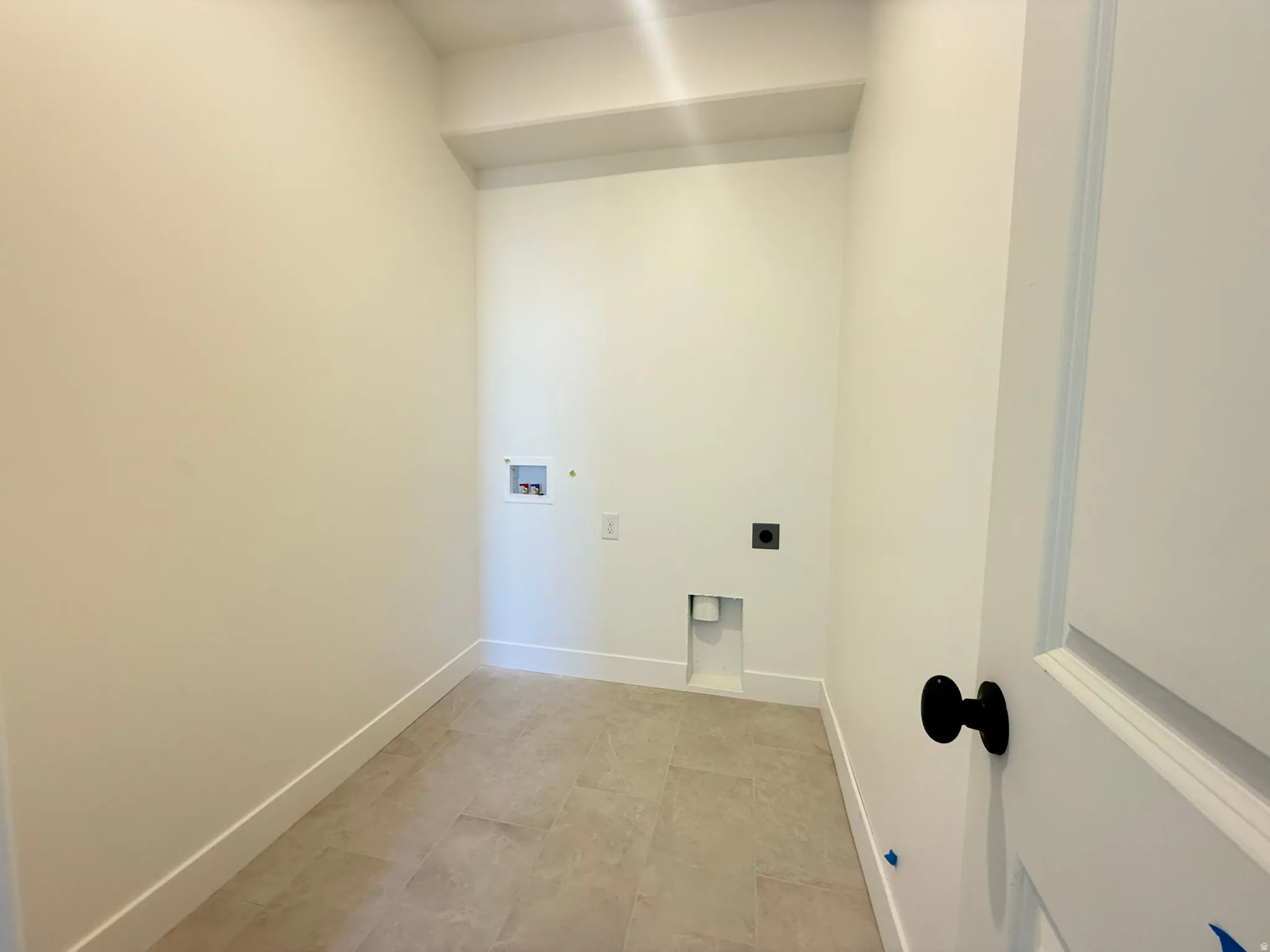 Laundry area with neutral toned tile flooring, white walls, and a white interior door with matte black hardware