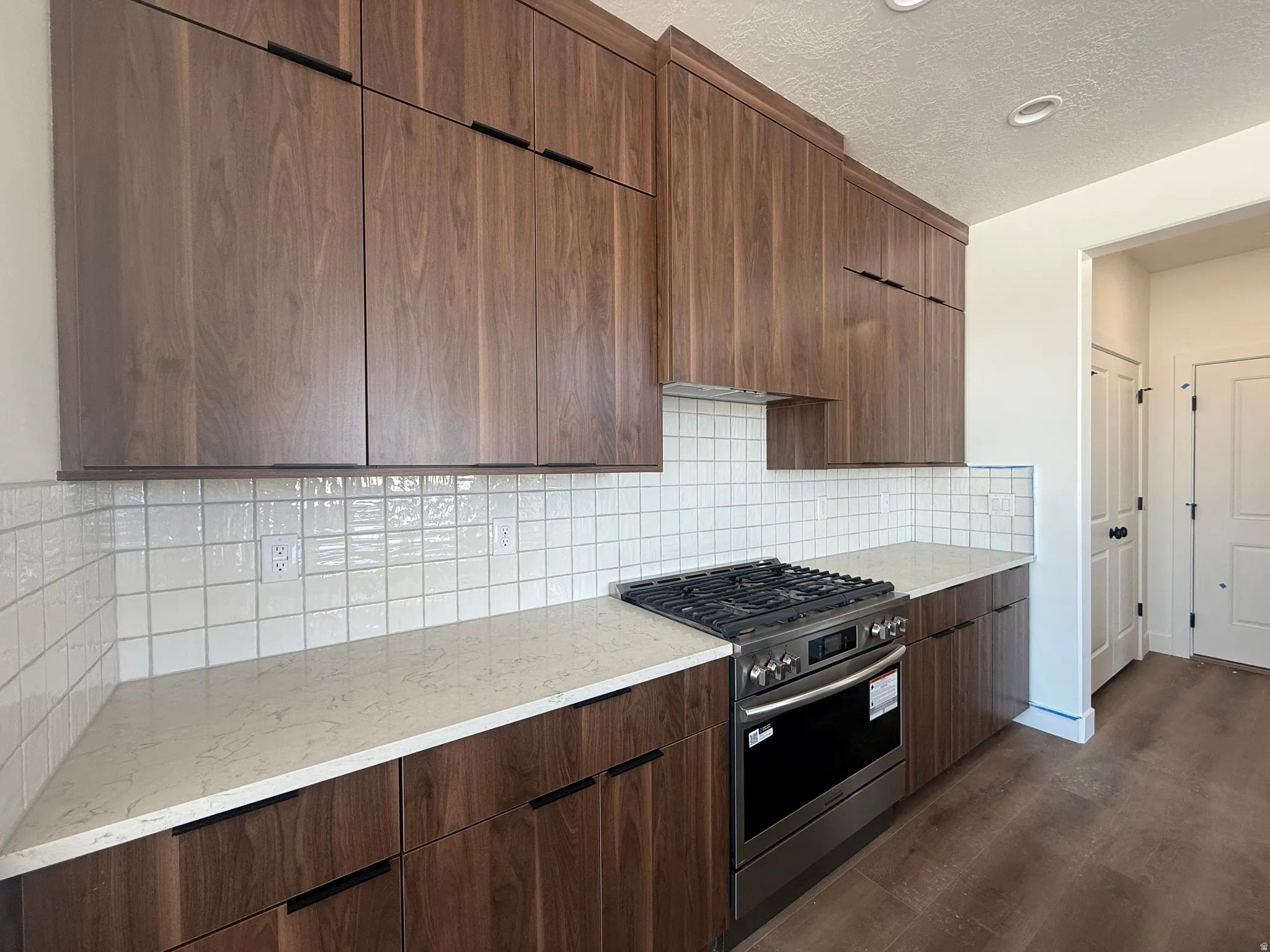 Modern kitchen featuring rich wood-finish cabinetry with black hardware, light-toned countertops, and a white square tile backsplash