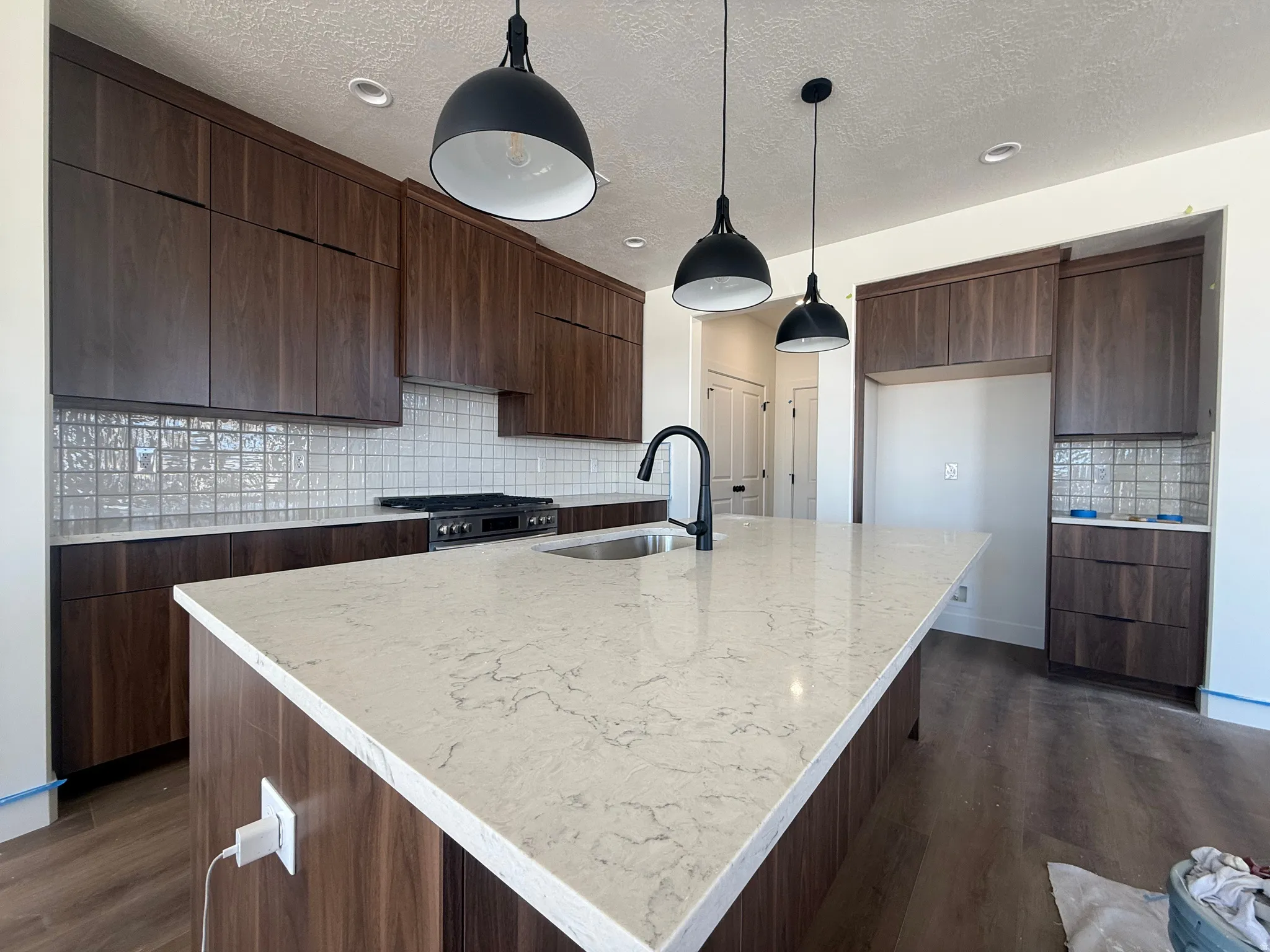 Kitchen featuring an expansive island with a light-toned countertop, dark wood-finish cabinetry, a patterned tile backsplash, and three pendant lights