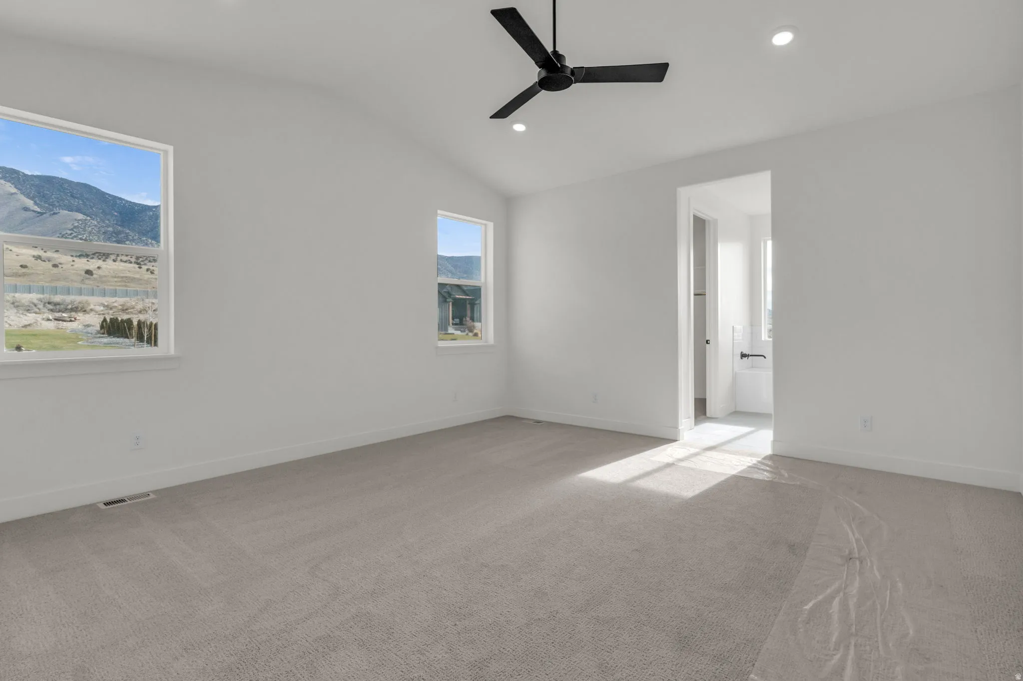 Primary bedroom with view windows, vaulted ceiling and ceiling fan.  Full-size walk-in closet as part of primary suite.