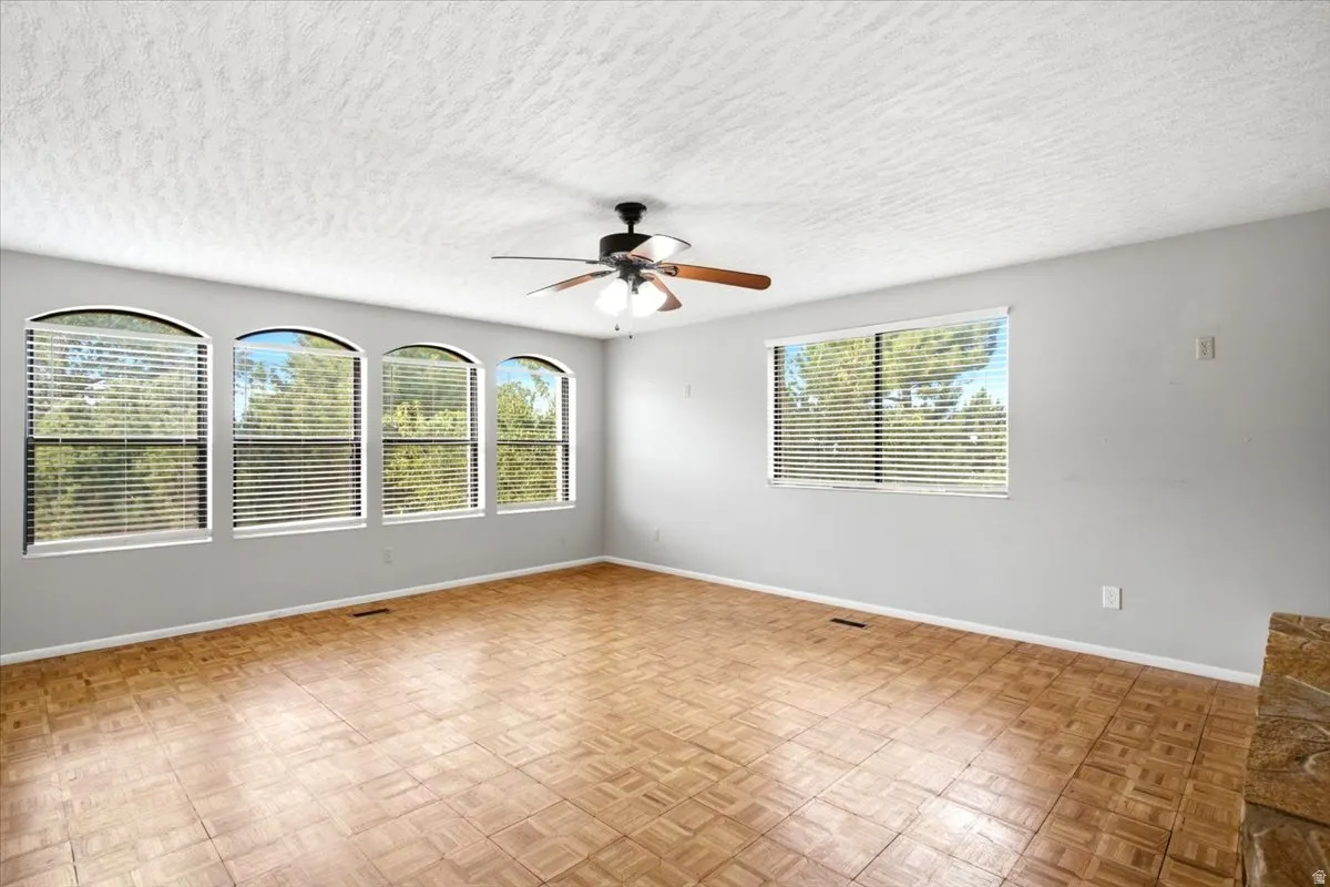 Spacious room featuring multiple arched windows, a large rectangular window, wood-finish parquet flooring, and a ceiling fan