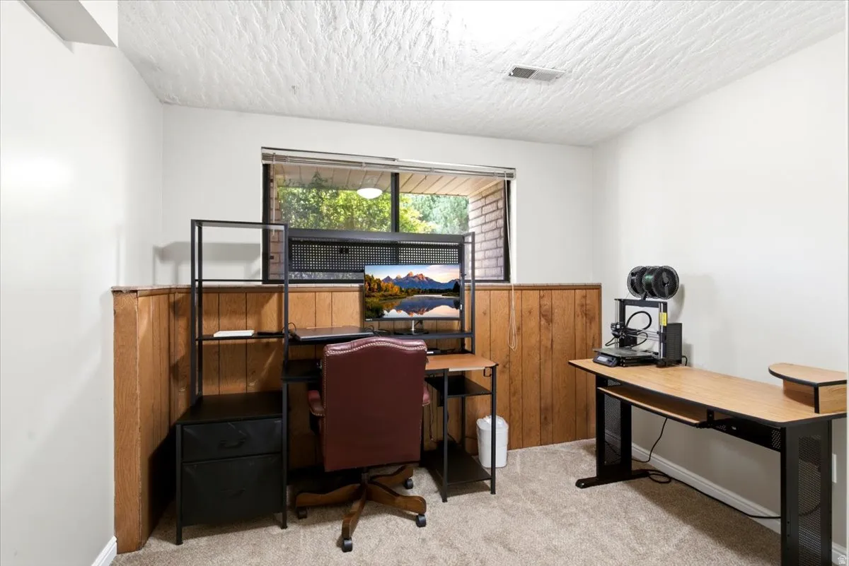 Room featuring light gray walls, wood paneling, a window with exterior brickwork, and a textured white ceiling