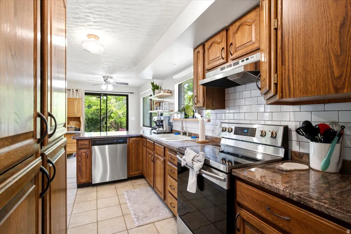 Kitchen featuring wood cabinetry, stainless steel appliances, subway tile backsplash, and stone countertops