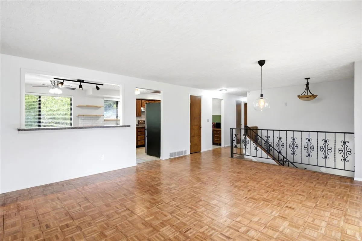 Parquet wood-finish flooring, white walls, black wrought iron stair railing, pass-through opening with countertop, and recessed lighting