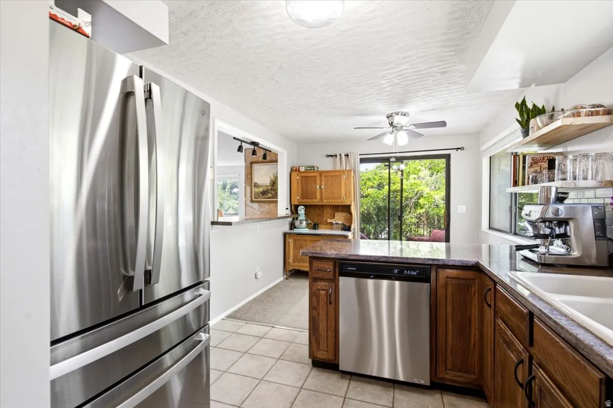 Kitchen featuring stainless steel appliances, tile flooring, wood cabinetry, stone countertops, and a sliding glass door