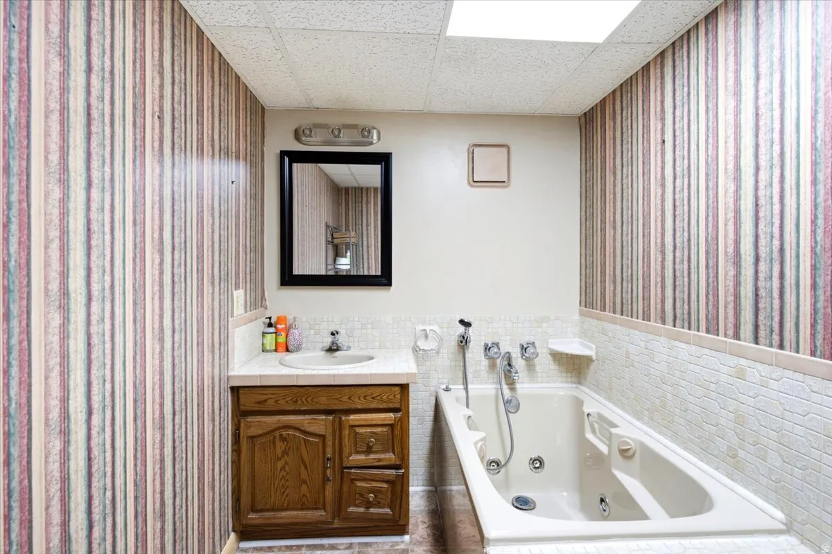 Bathroom featuring a built-in jetted tub, wood-finish vanity with an integrated sink, vanity mirror, and recessed ceiling lighting