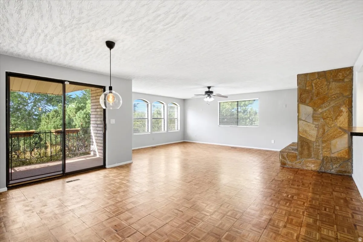 Wood-finish flooring, stone-clad fireplace, sliding glass door to a balcony with decorative railing, multiple arched windows, and a ceiling fan