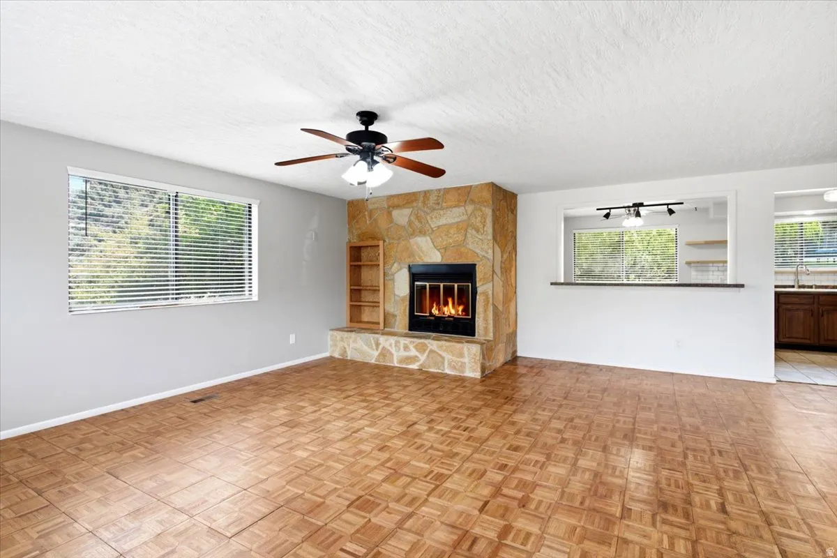 Wood-finish flooring, stone-clad fireplace with hearth, built-in shelving, ceiling fan with light, and a pass-through window with bar seating