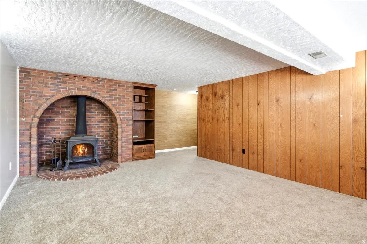 Brick fireplace with an arched opening, built-in shelving, wood-paneled accent wall, and neutral carpeting