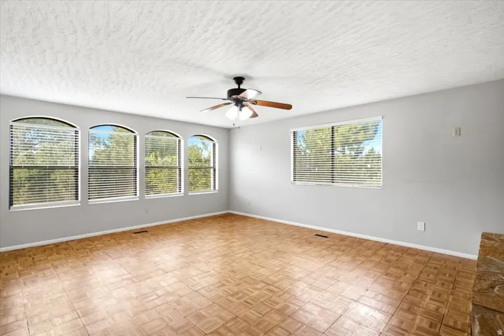 Spacious room featuring multiple arched windows, a large rectangular window, wood-finish parquet flooring, and a ceiling fan