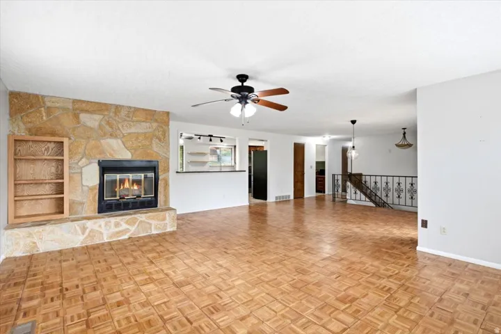 Living area with stone-clad fireplace and hearth, built-in shelving, wood-finish parquet flooring, and ceiling fan