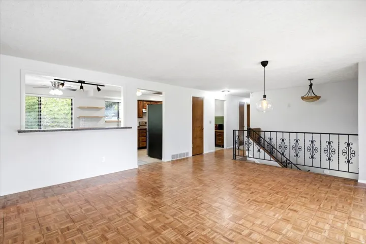 Parquet wood-finish flooring, white walls, black wrought iron stair railing, pass-through opening with countertop, and recessed lighting