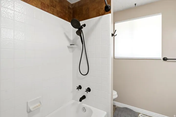 Bathroom featuring a white subway tile surround, textured accent tile, and a tub with matte black fixtures