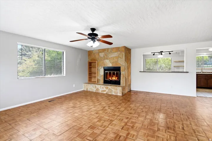 Wood-finish flooring, stone-clad fireplace with hearth, built-in shelving, ceiling fan with light, and a pass-through window with bar seating