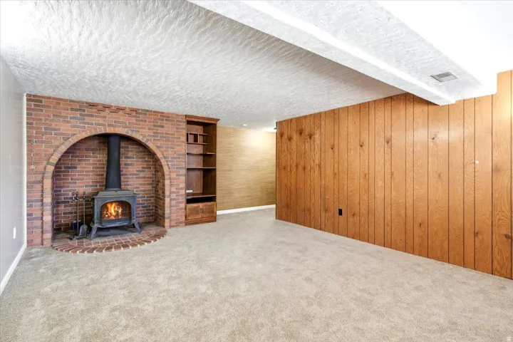 Brick fireplace with an arched opening, built-in shelving, wood-paneled accent wall, and neutral carpeting