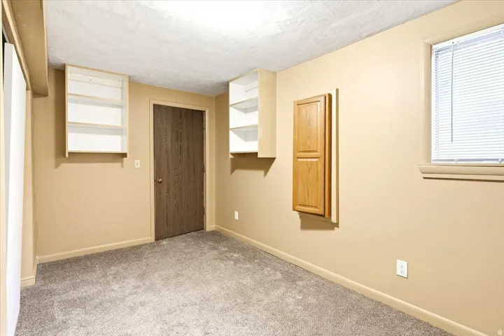 Neutral wall paint, textured ceiling, light gray carpet, wood-finish door, and a built-in wood-panel cabinet