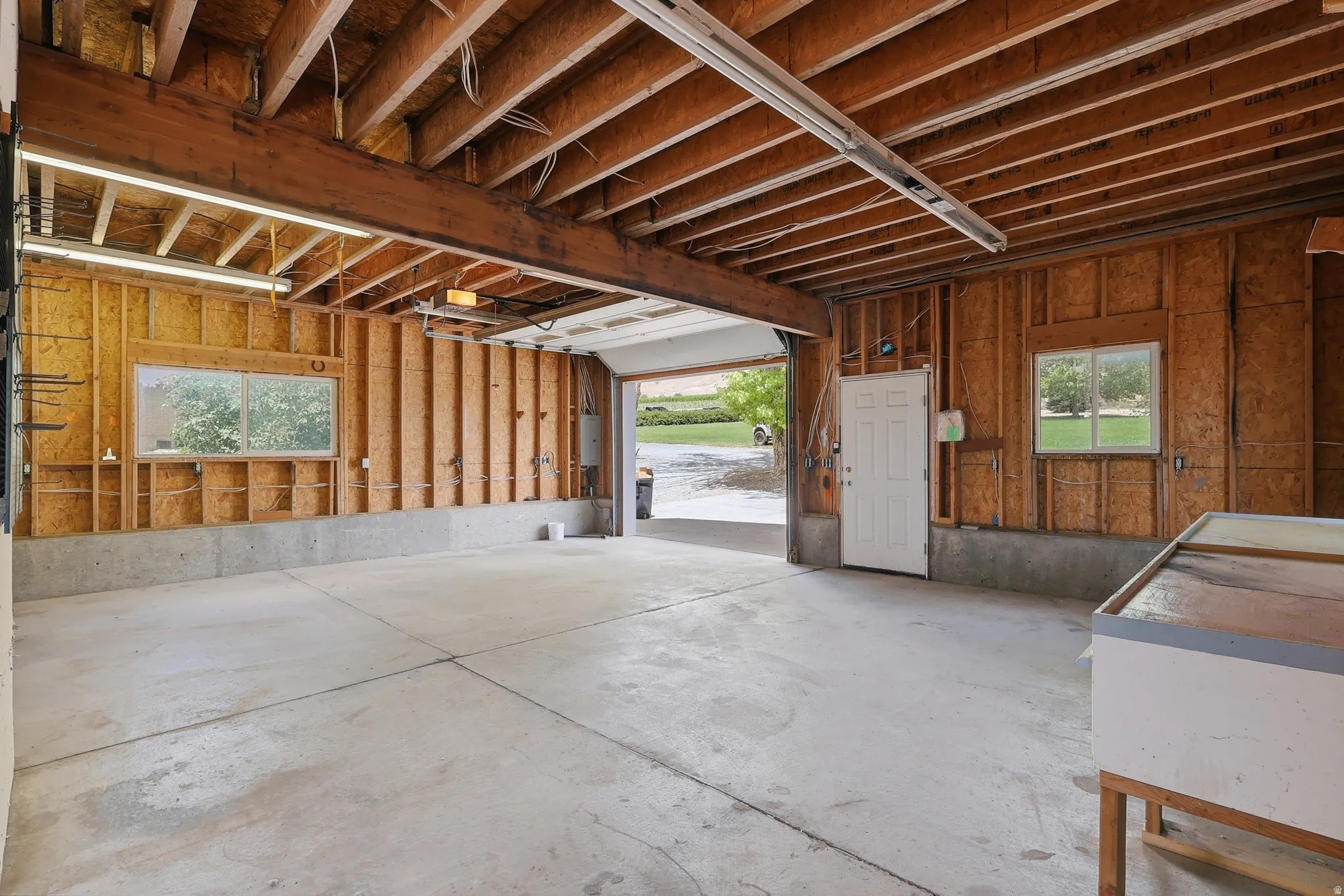 Spacious garage featuring exposed wood beam ceiling, concrete flooring, dual windows, and an overhead garage door