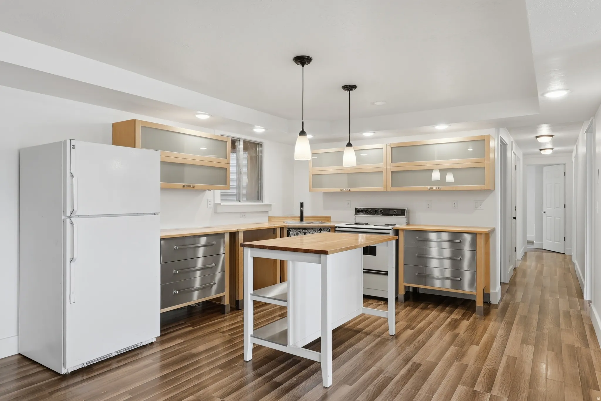 Kitchen featuring wood-finish flooring, light wood upper cabinetry with frosted glass inserts, and stainless steel lower cabinetry