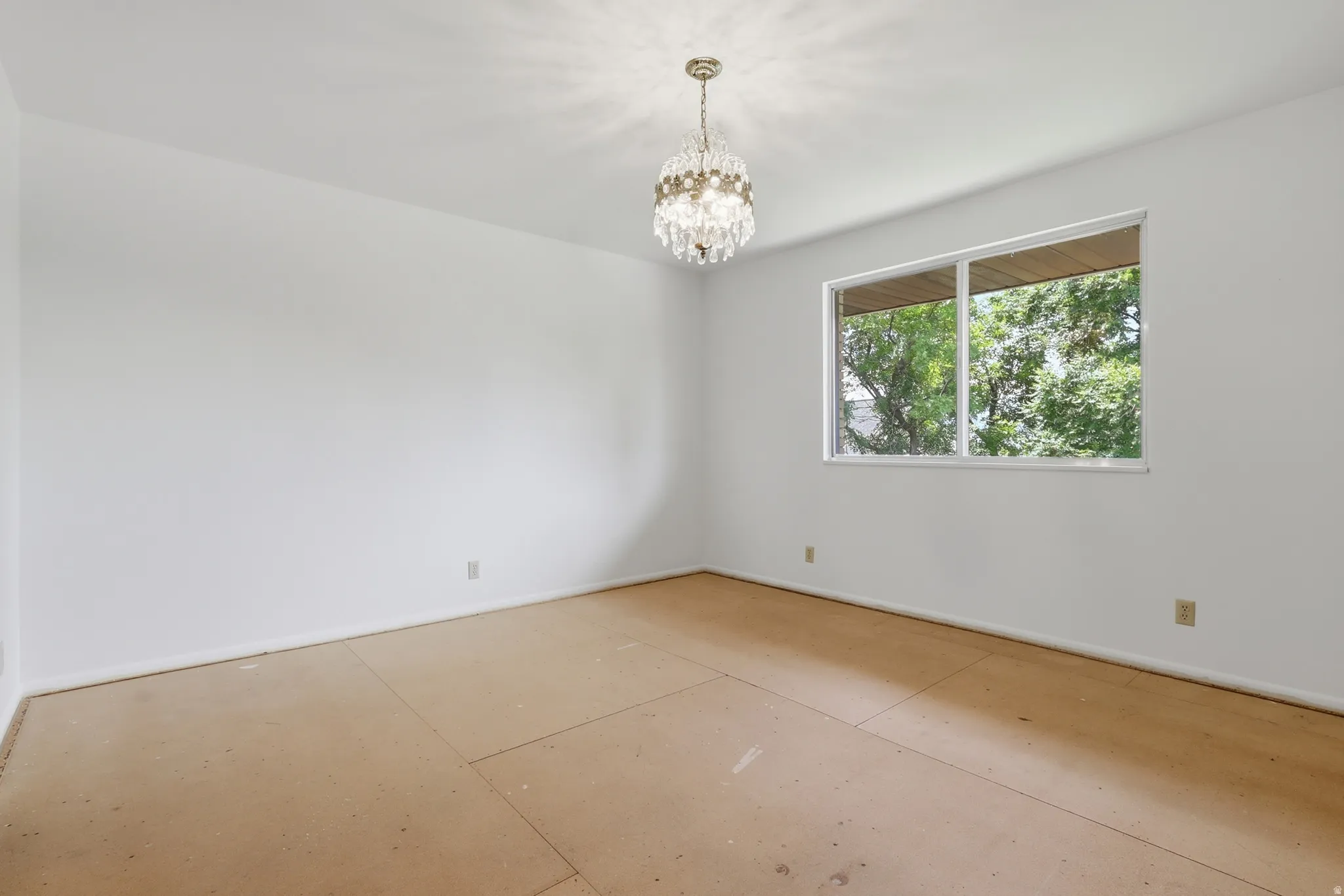 Bright interior space featuring a dual-pane window, a crystal chandelier, white walls, and subflooring