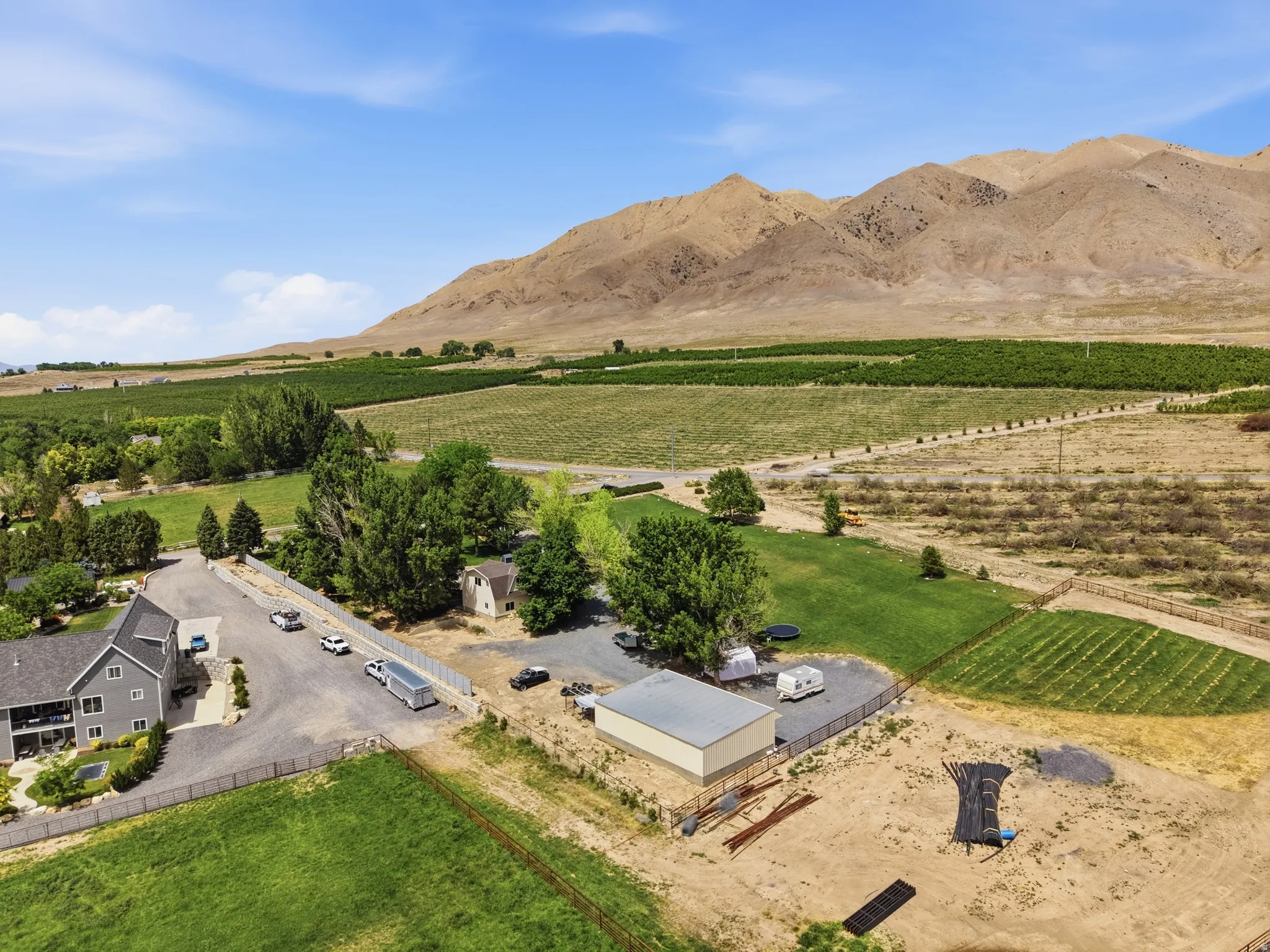 Expansive property featuring a gray multi-story residence with a lower-level patio, multiple outbuildings, and extensive cultivated acreage