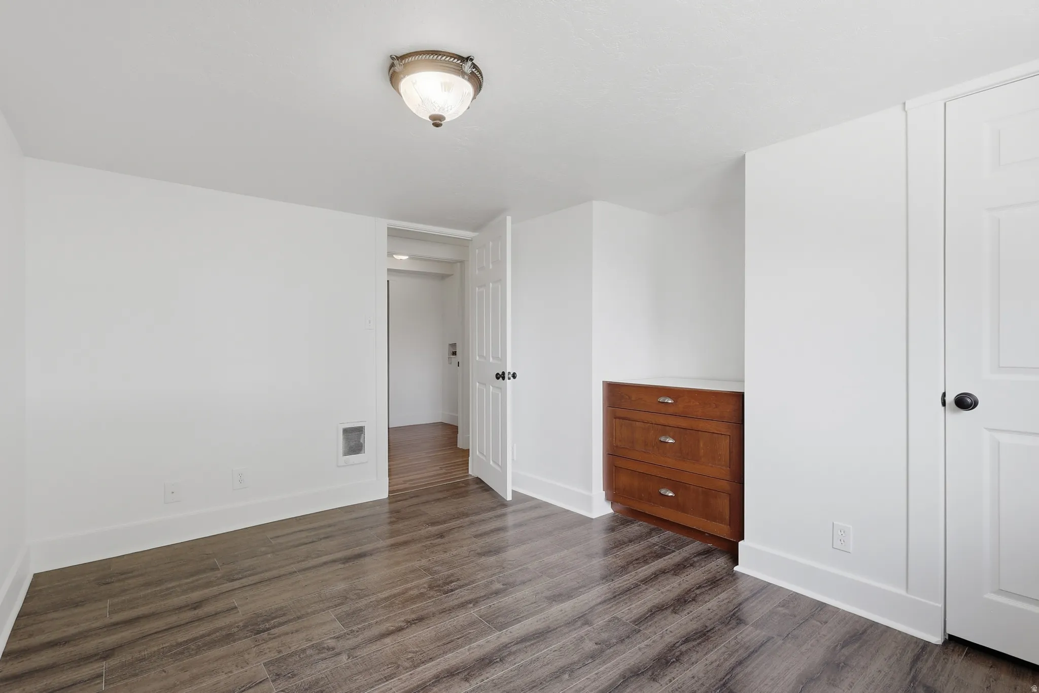 Interior room featuring wood-finish flooring, white walls, and a built-in wood-tone dresser with three drawers