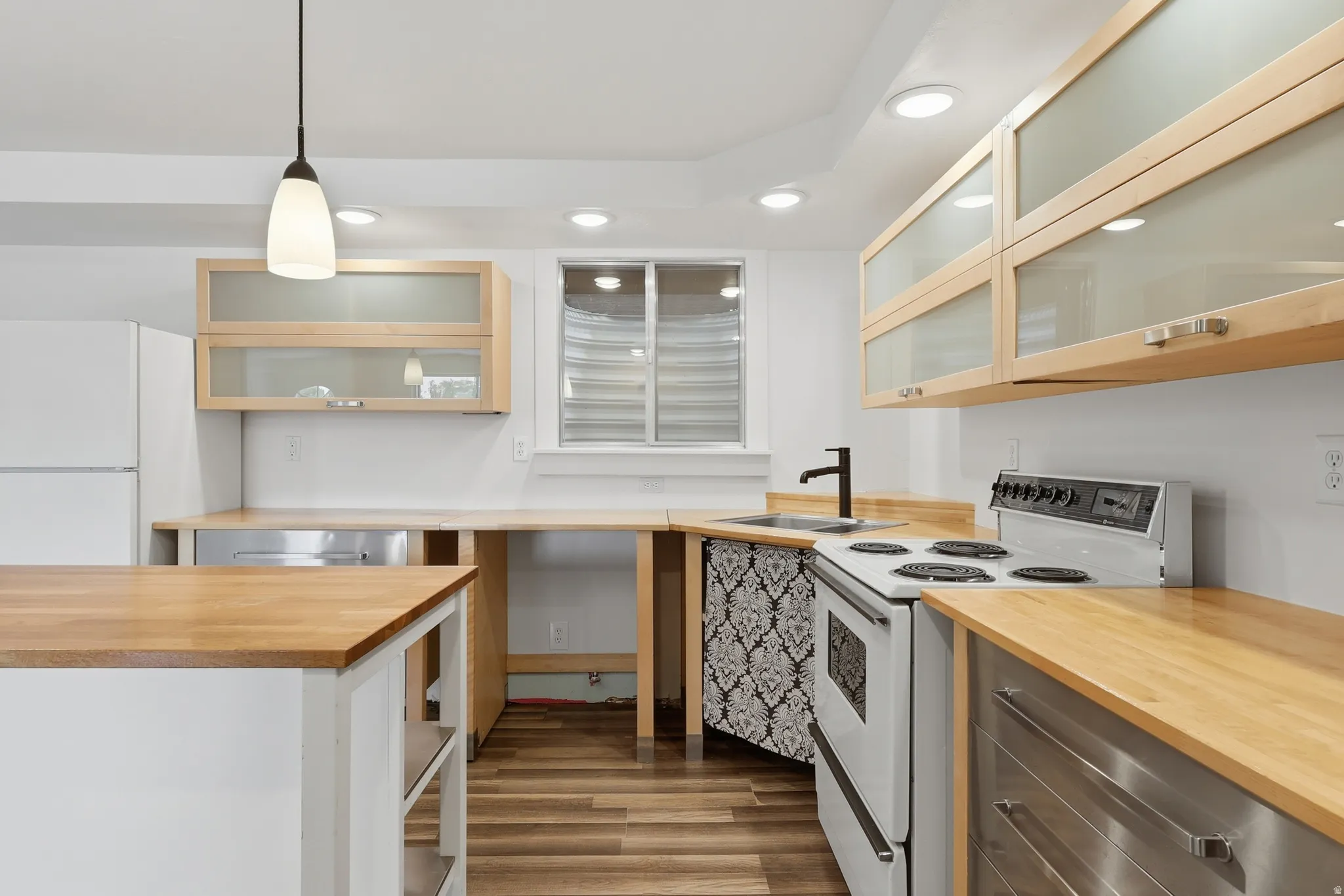 Kitchen featuring light wood-finish cabinetry with frosted glass inserts, wood-finish countertops, stainless steel appliances, and wood-finish flooring