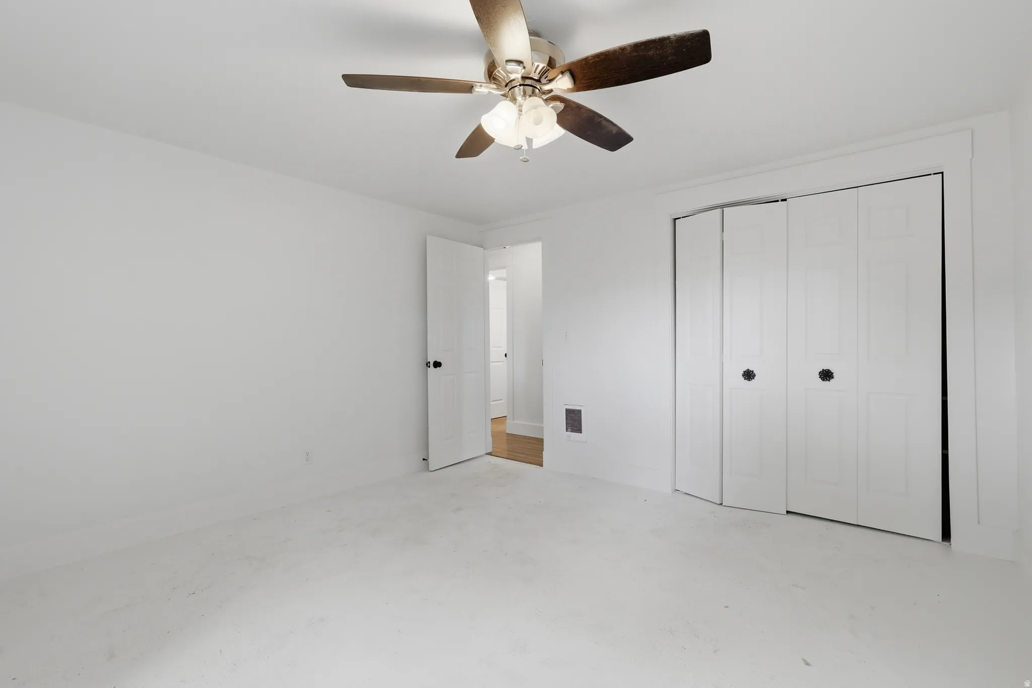 Room featuring white walls and ceiling, a ceiling fan with light fixture, carpeted flooring, a panel door, and bi-fold closet doors