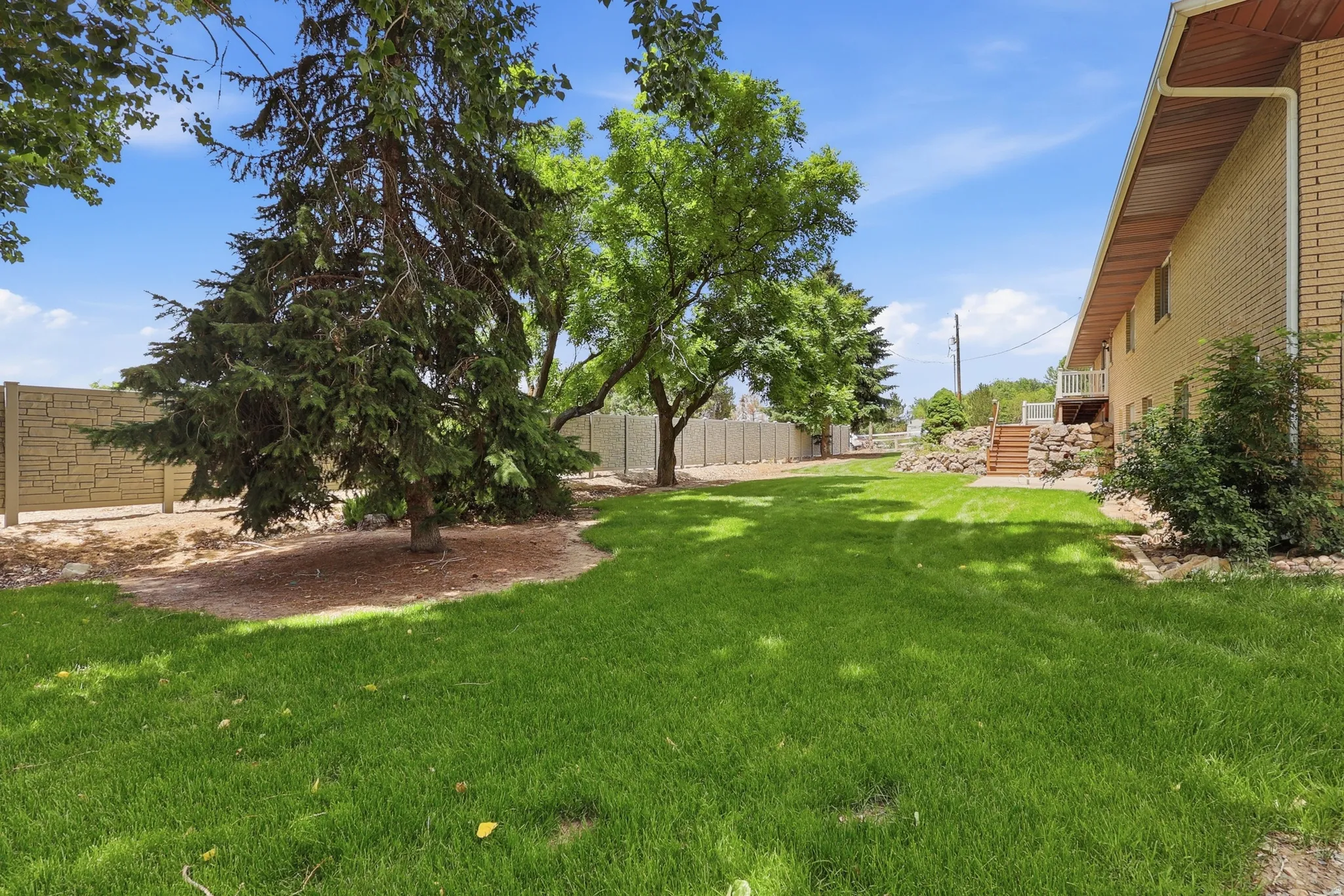 Expansive lawn area featuring mature trees, a decorative stone-patterned fence, and a brick exterior building with a wood-soffit overhang